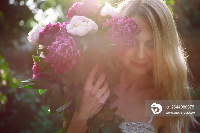 girl in the garden with a big bouquet of peonies in hands at sunset