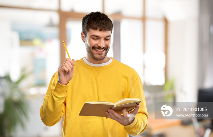 inspiration, idea and people concept - smiling young man in yellow sweatshirt with diary and pencil over office background