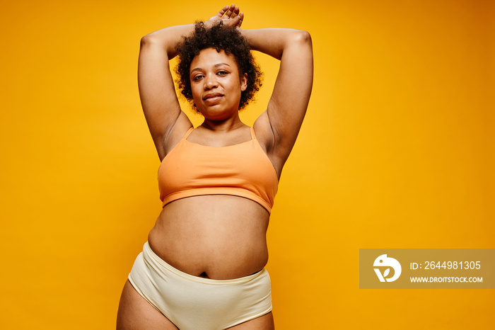 Waist up portrait of confident black woman wearing underwear against vibrant yellow background, copy space