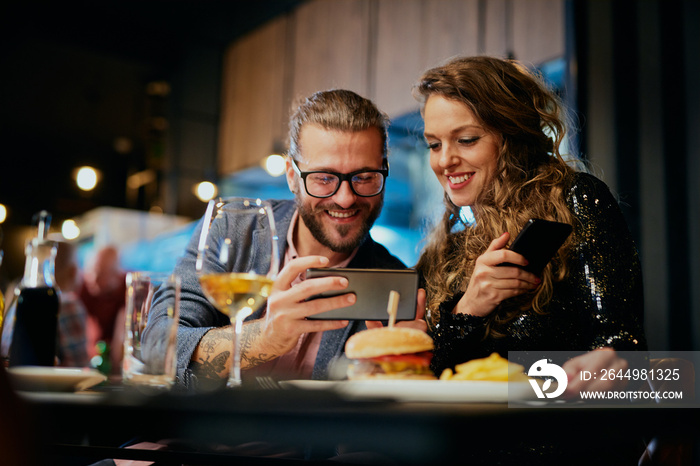 Cute caucasian fashionable couple sitting in restaurant at dinner and taking selfie.