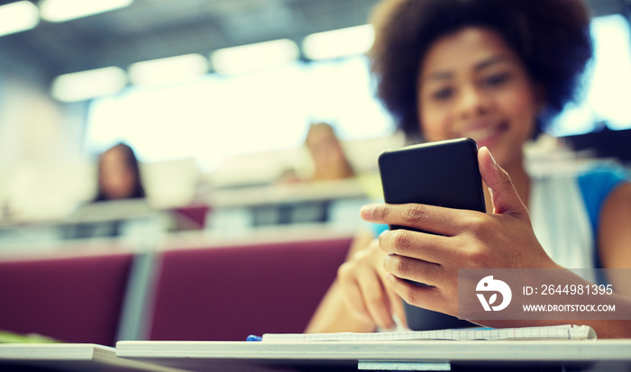 education, high school, university, learning and people concept - close up of happy african student girl with smartphone at lecture hall