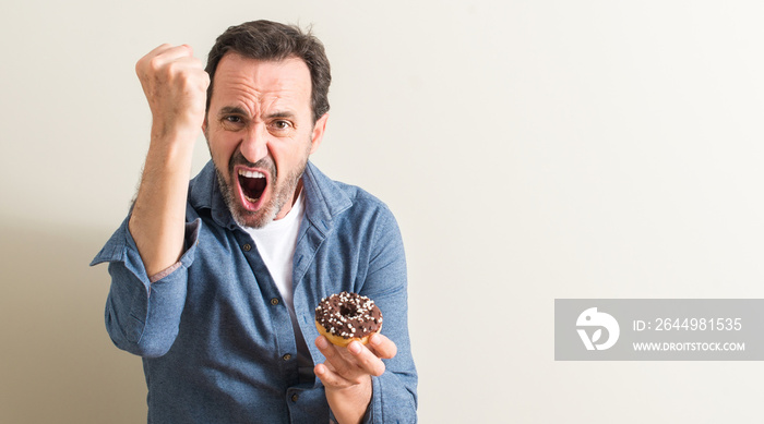 Senior man eating chocolate donut annoyed and frustrated shouting with anger, crazy and yelling with raised hand, anger concept