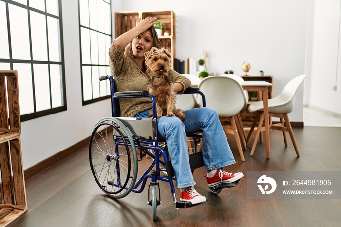 Young hispanic girl sitting on wheelchair at home showing arms muscles smiling proud. fitness concept.