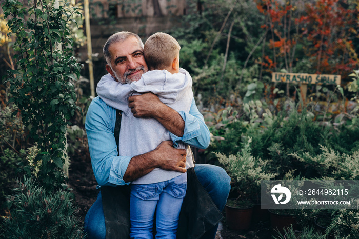 little boy embracing with his grandfather in their plant nursery