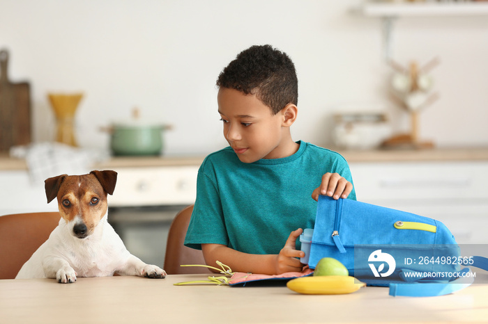 Cute little boy with funny dog putting his school lunch in bag