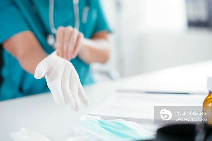 Young female doctor in medical office. Close up of female doctor putting gloves on.