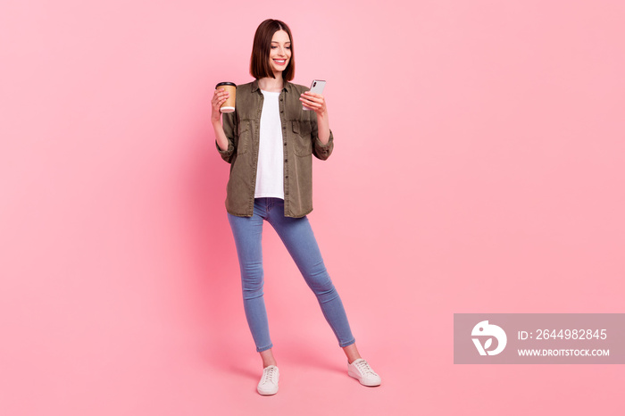 Full body photo of funny brunette hairdo lady look telephone hold coffee wear green shirt jeans isolated on pink color background