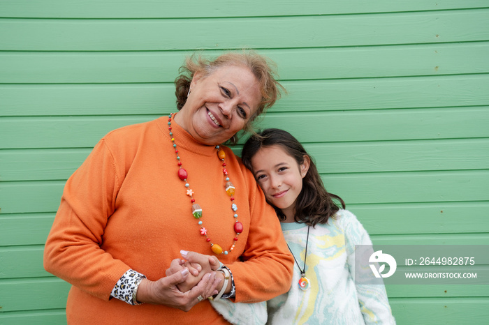 Portrait of grandmother standing with granddaughter against green wall