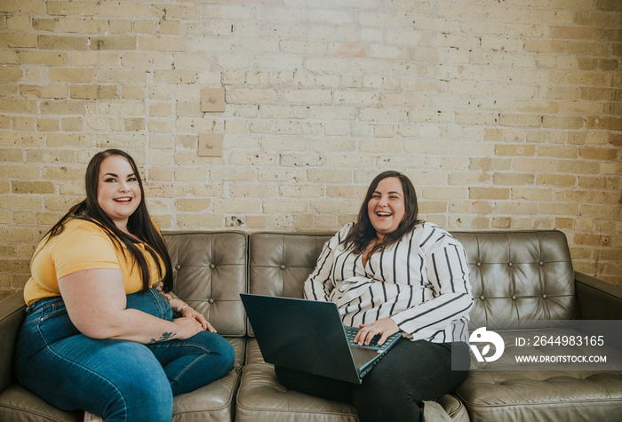 3 women sit on sofa laughing and working