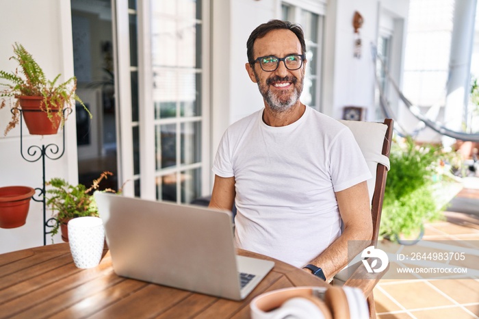 Middle age man using computer laptop at home smiling looking to the side and staring away thinking.