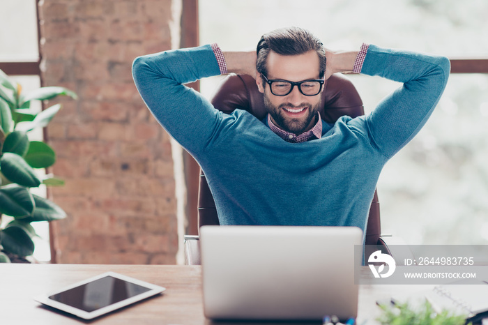 Stunning, harsh, virile, joyful man holding two hands behind the head, watching movie, video on laptop, having fun during break time, looking at screen of computer, sitting at desk in work place