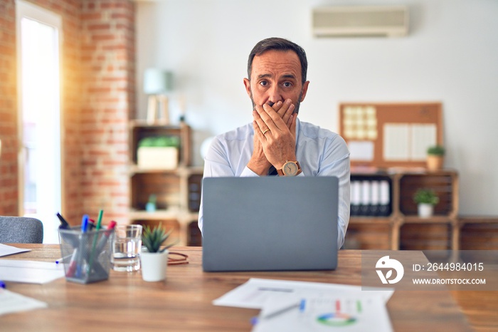 Middle age handsome businessman wearing tie sitting using laptop at the office shocked covering mouth with hands for mistake. Secret concept.