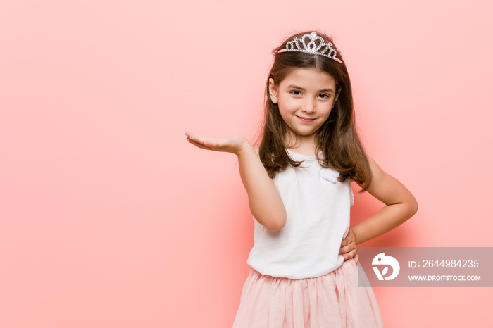 Little girl wearing a princess look showing a copy space on a palm and holding another hand on waist.