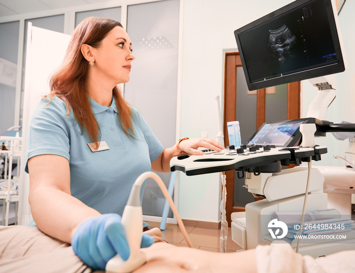 Female sonographer examining woman with ultrasound scanner. Doctor looking at display while doing ultrasound examination. Concept of healthcare, medical examination and ultrasound diagnostics.