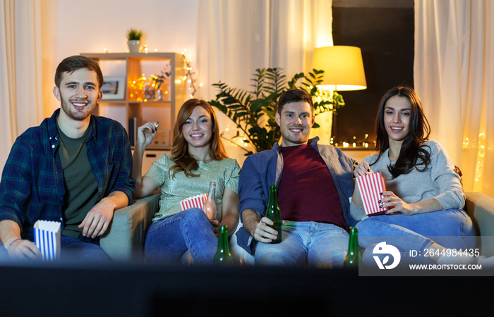 friendship and leisure concept - happy friends with beer and popcorn watching tv at home at night