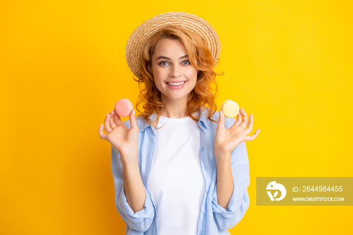 Cute young woman hold macaroon. Diet, dieting concept. Beautiful smiling young girl eating colorful macaroons over yellow background.