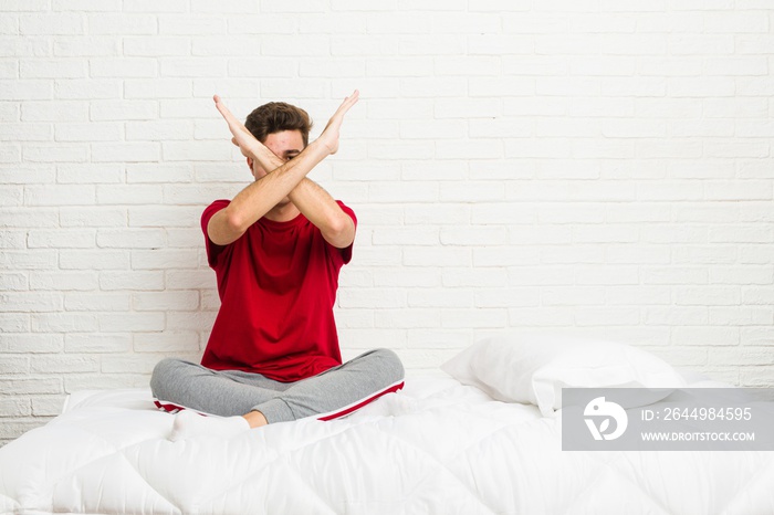 Young teenager student man on the bed keeping two arms crossed, denial concept.