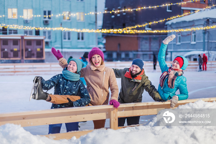 Happy group of multiracial friends have fun skating on an outdoor ice rink. Concept of communication and new year