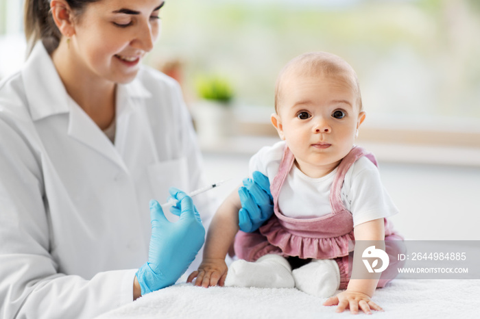 medicine, healthcare and vaccination concept - female pediatrician doctor or nurse with syringe making injection of vaccine for baby girl patient at clinic or hospital