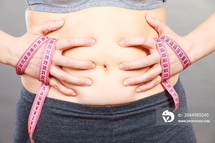 Woman touching stomach holding measuring tape