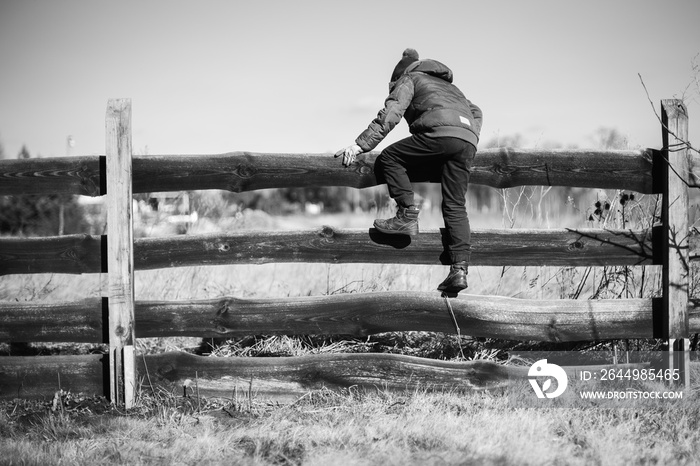 Young boy walks over a wooden fence