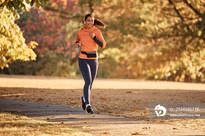 Happy female athlete running while exercising in nature during autumn day.