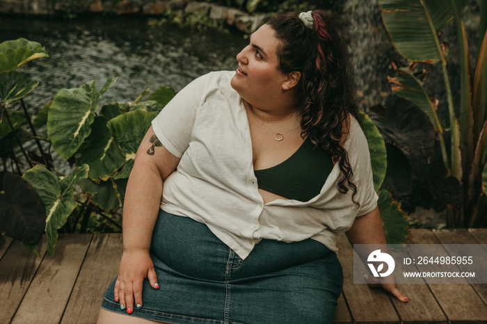 plus size woman sits on bench beside pond