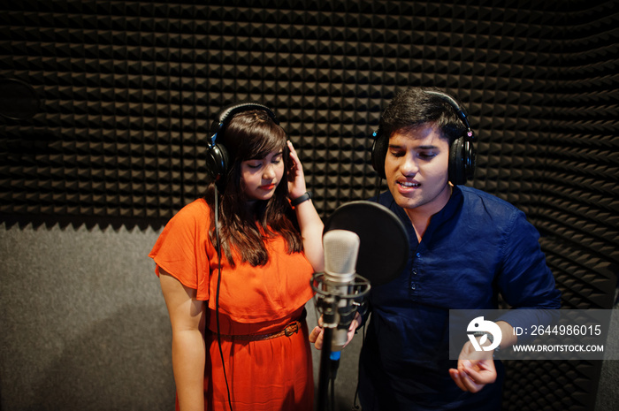 Young asian duet singers with microphone recording song in record music studio.