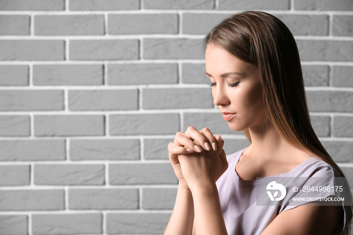 Religious young woman praying against brick wall