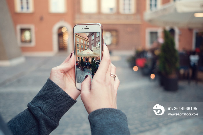 Back close up view of female person holding cellphone with and make photo. Woman’s hands with mobile phone devise, finger touching display