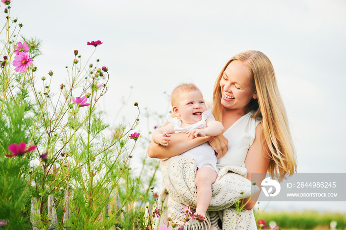 Happy young mother playing with baby girl in flower garden on a nice sunny day