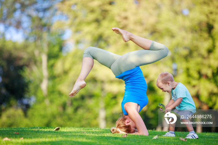 Young woman working out outdoors, little son playing beside her