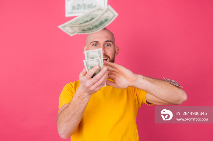 European man on pink red background with fan on 100 dollars happy excited throwing in air isolated space
