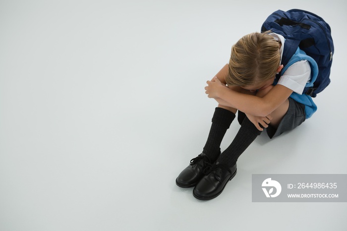 Sad schoolboy sitting on white background