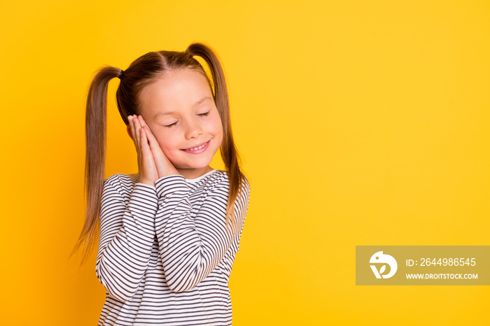 Portrait of young happy smiling girl child kid daydreaming with closed eyes hold hands together isolated on yellow color background