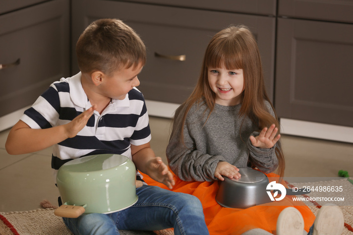 Cute little musicians playing drums on kitchenware at home