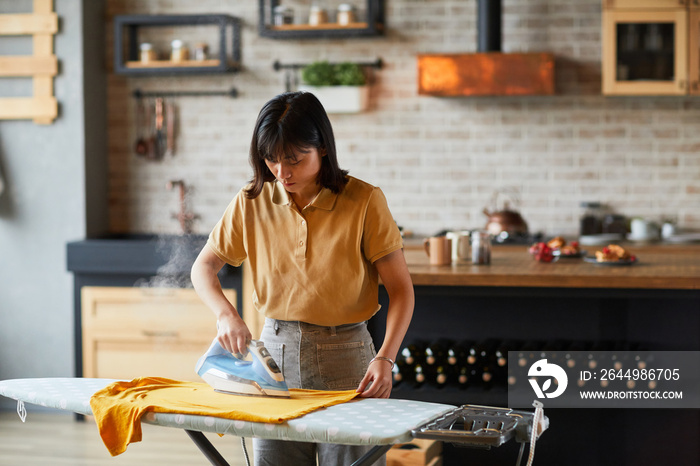 Waist up portrait of young Asian woman ironing clothes at home and doing household chores, copy space