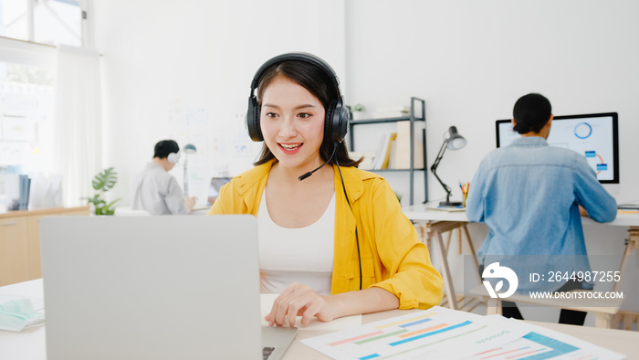 Asia businesswoman social distancing in new normal situation for virus prevention while using laptop presentation to colleagues about plan in video call while work in office. Life after corona virus.