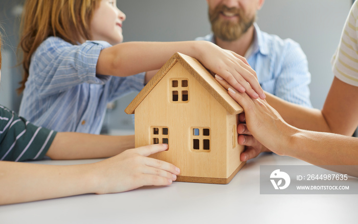 Family with little kids planning to move, relocate, buy new home, take loan, refinance mortgage, or get insurance. Group of mom, dad and sons together holding small, miniature wooden house, closeup