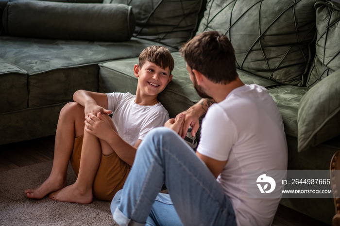 Father and son sit on the living room floor and talk, the son liked the story and smiled