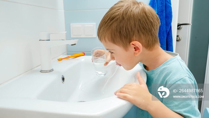 Portrait of smiling toddler boy rinsing mouth with water from glass after brushing and cleaning teeth with toothbrush and toothpaste. Concept of teeth hygiene and daily routine