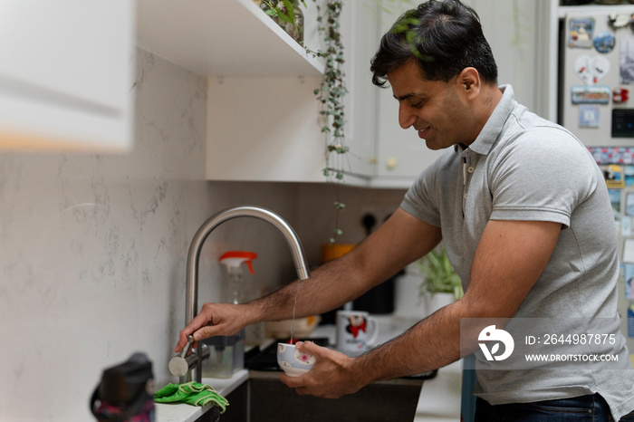 Man washing dishes in kitchen sink