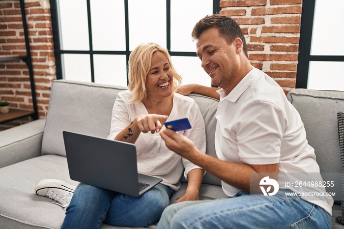 Middle age man and woman using laptop and credit card sitting on sofa at home