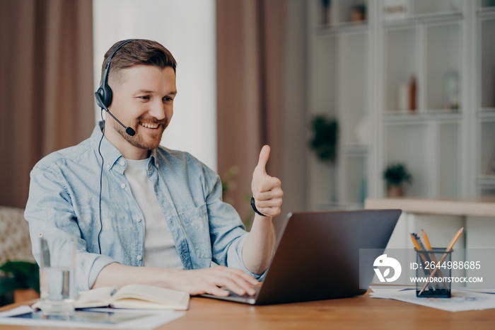 I like it. Glad bearded adult man has video conference keeps thumb up likes something focused at laptop computer has distance job interview dressed casually. Professional call center agent working