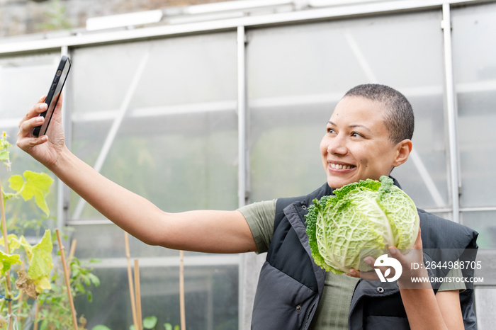 Smiling woman taking selfie with homegrown cabbage in allotment