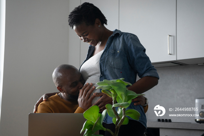 Man kissing pregnant woman’s belly in kitchen