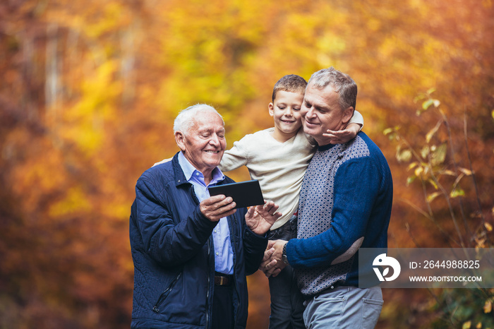 Elderly father adult son and grandson out for a walk in the park, using digital tablet.