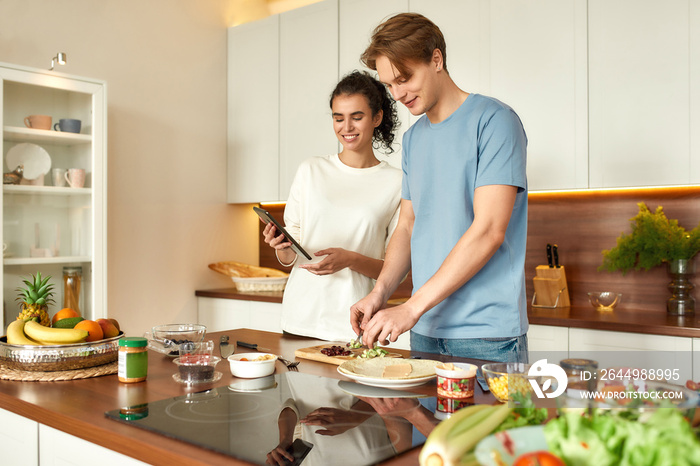 Fitter, healthier, happier. Young man cutting vegetables while woman checking recipe on the digital tablet. Vegetarians cooking breakfast in the kitchen together. Vegetarianism, healthy food concept