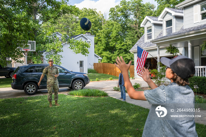 Air Force service member plays catch with sons after coming home from work in uniform.