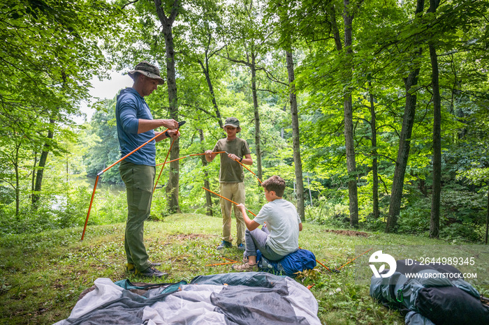 Air Force service member sets up a tent with his sons on  a backpacking trip.